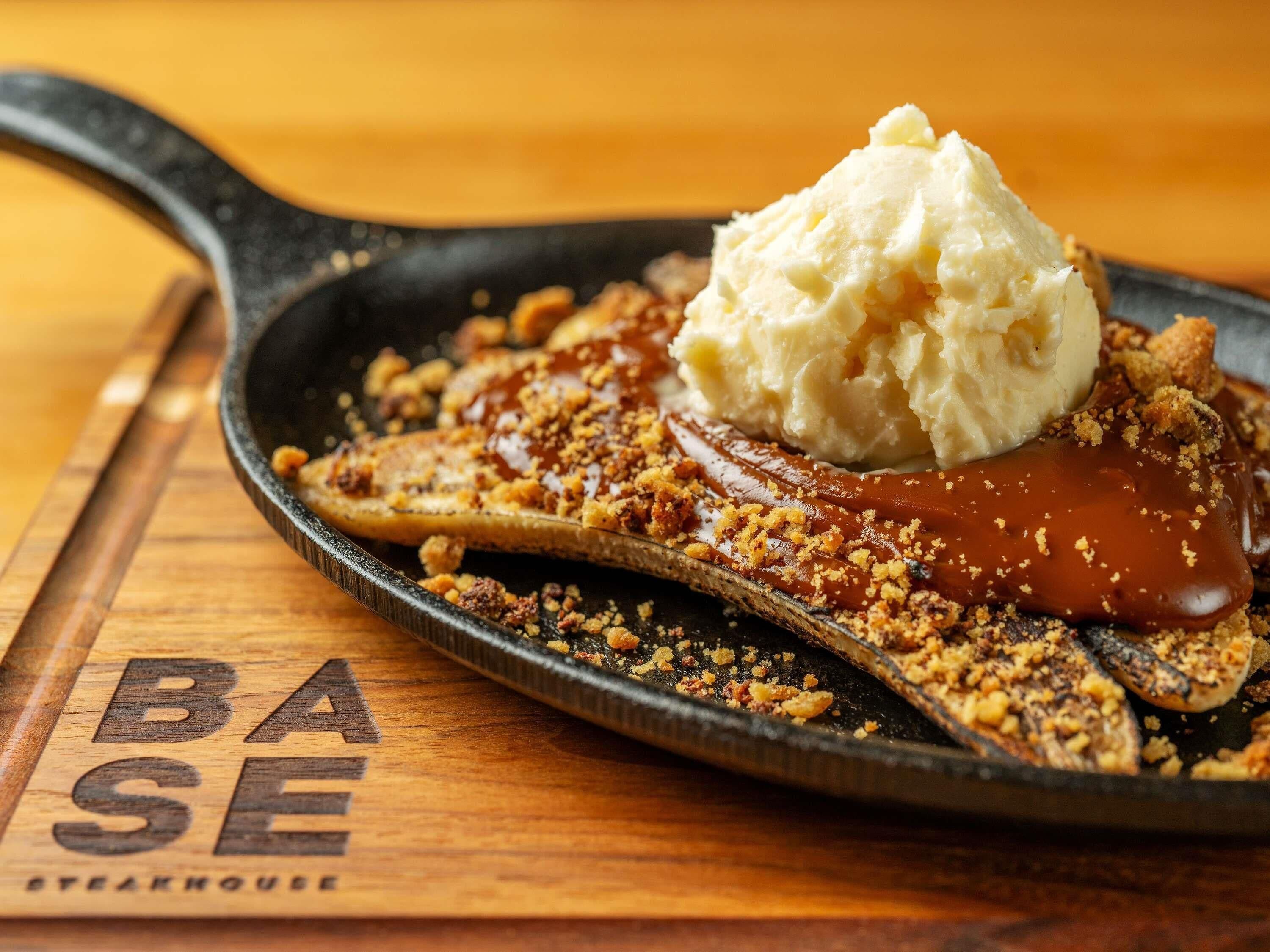 Una sartén con un postre de salsa de caramelo, cobertura desmenuzada y una bola de helado de vainilla.