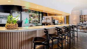A bar area with stools, a counter, and a refrigerator with a logo. - Pullman São Paulo Guarulhos Airport (Guarulhos)
