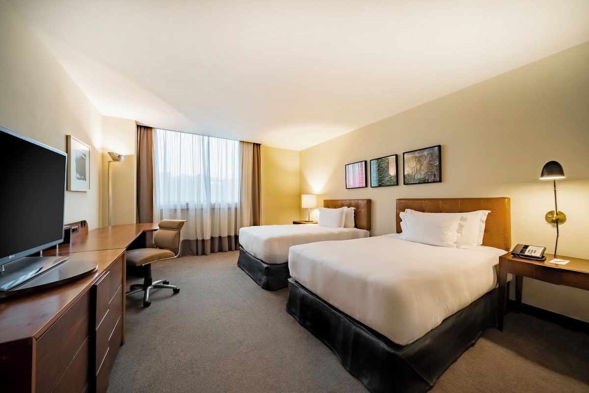 Habitación de hotel con dos camas, un escritorio con televisor, una silla y una lámpara.