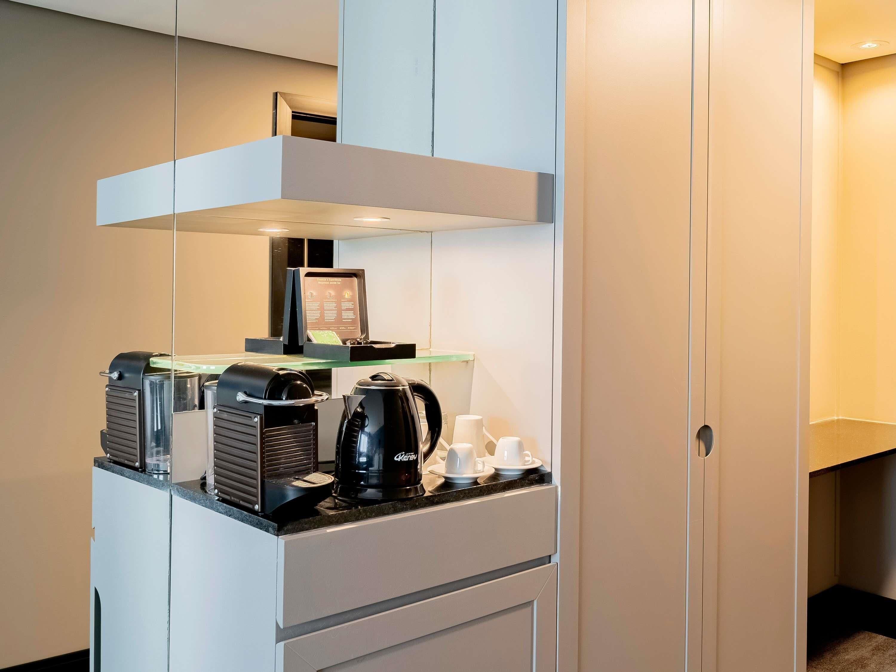 A compact kitchenette with a coffee machine, a kettle, and a small refrigerator.