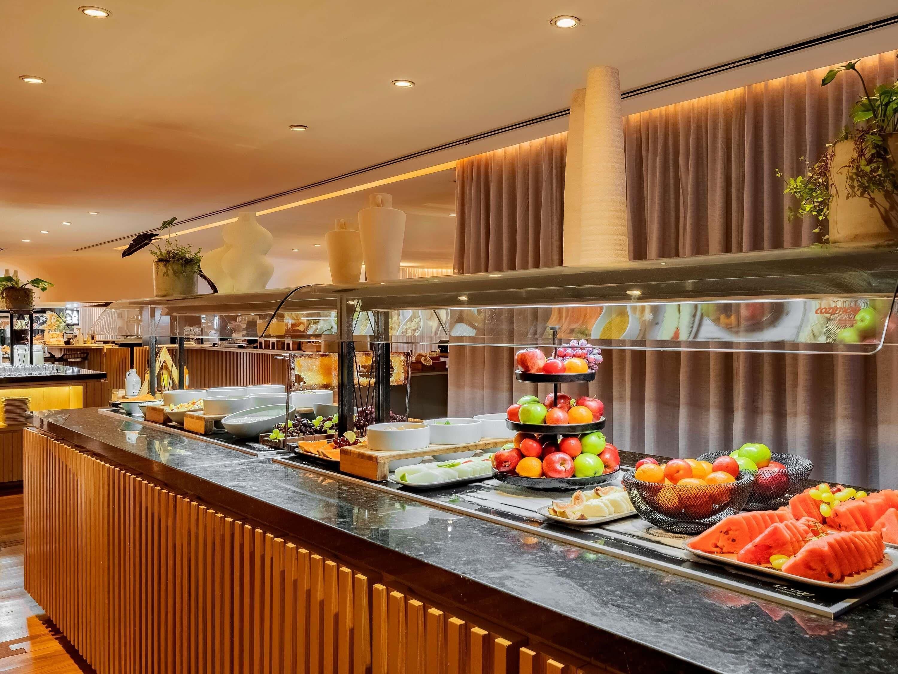 Un mostrador de buffet con diversas frutas y platos, un diseño de panel de madera y un techo moderno con iluminación empotrada.