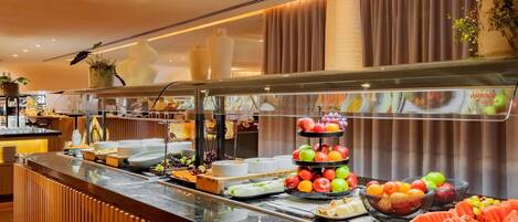 Un mostrador de buffet con diversas frutas y platos, un diseño de panel de madera y un techo moderno con iluminación empotrada.