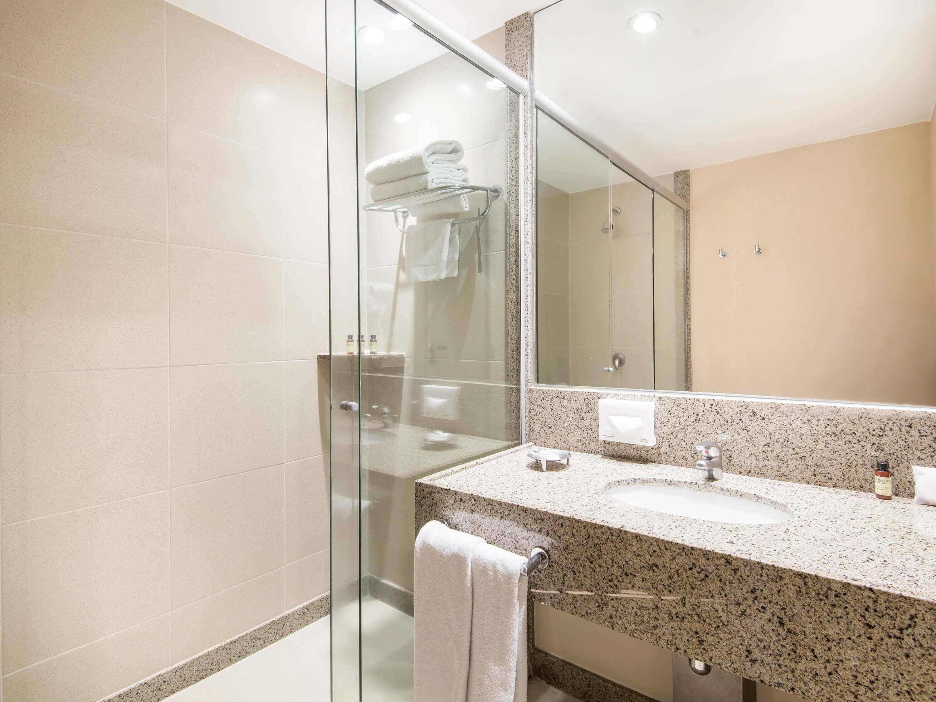 Une salle de bain moderne avec une douche à parois de verre, un lavabo sur un plan de travail en granit et un grand miroir.