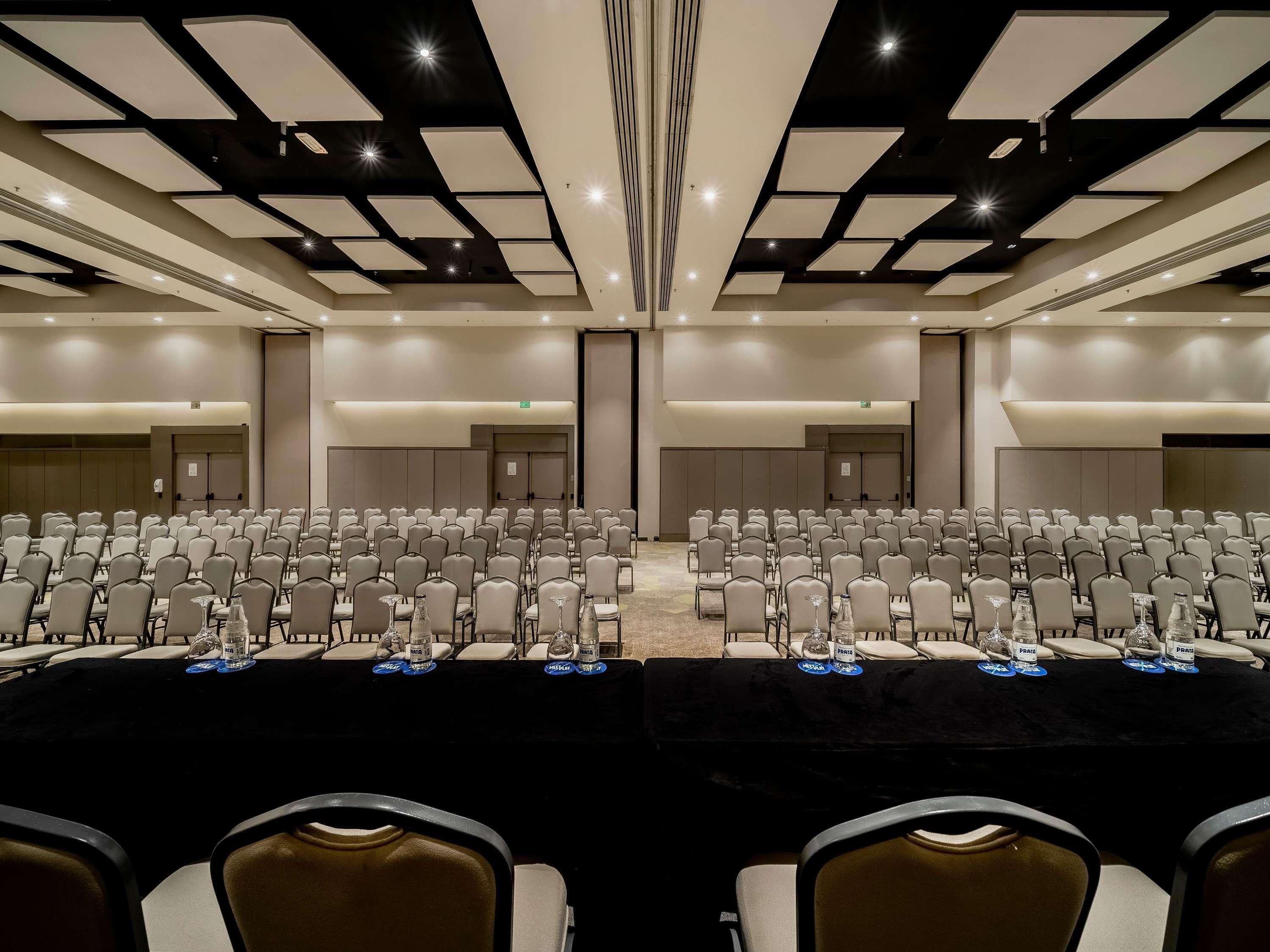 A conference room with rows of chairs, tables with water bottles, and a modern ceiling design.