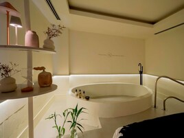 Un baño moderno con una bañera independiente, un estante con objetos decorativos y un toallero de pared.