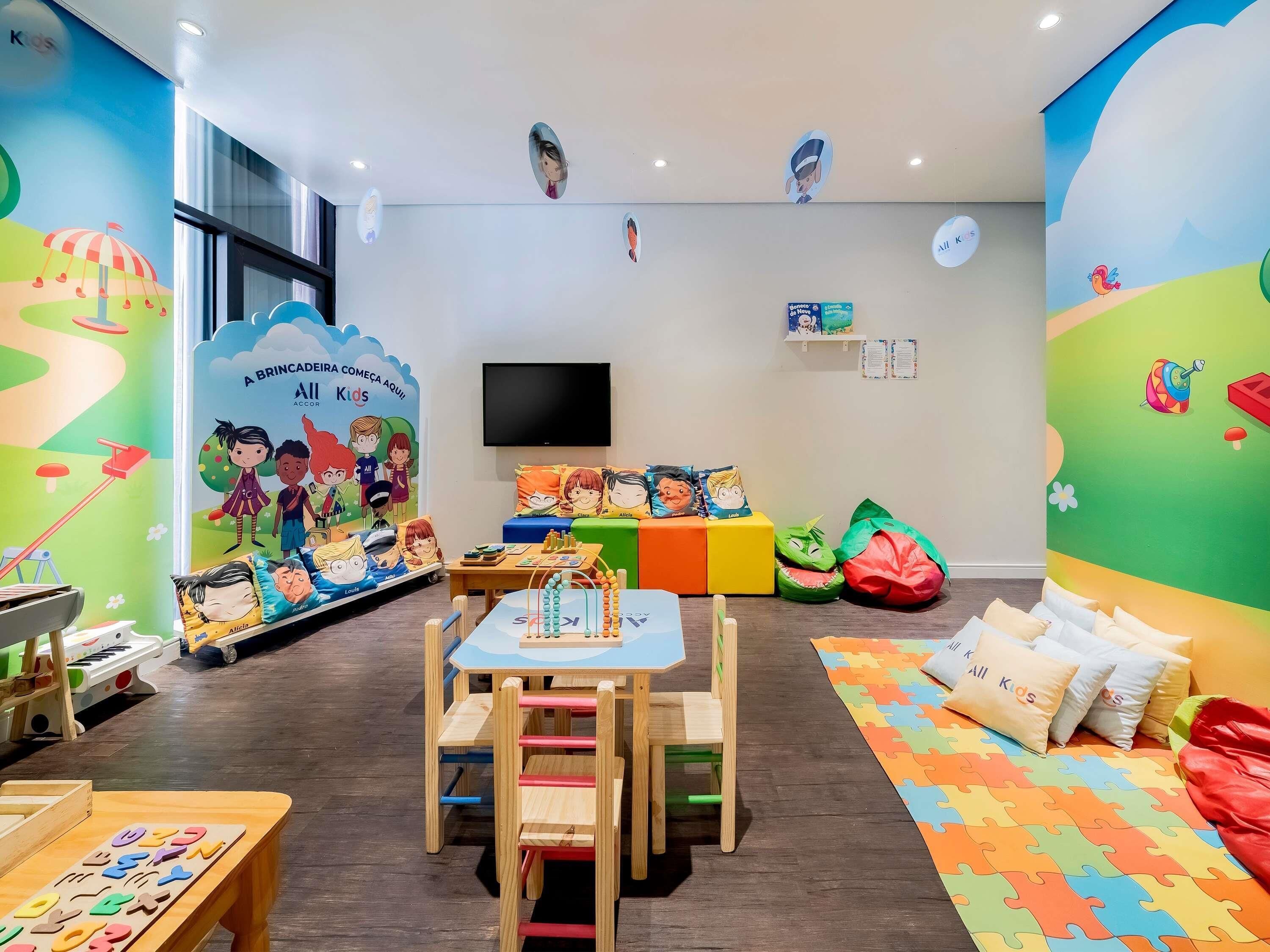 Un cuarto de juegos infantil con un mural grande, un televisor, y varios juegos de llano y juguetes.