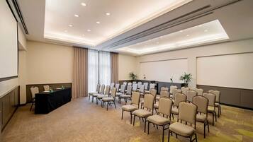 A conference room with a long table, rows of chairs, a projector screen, and a carpeted floor.