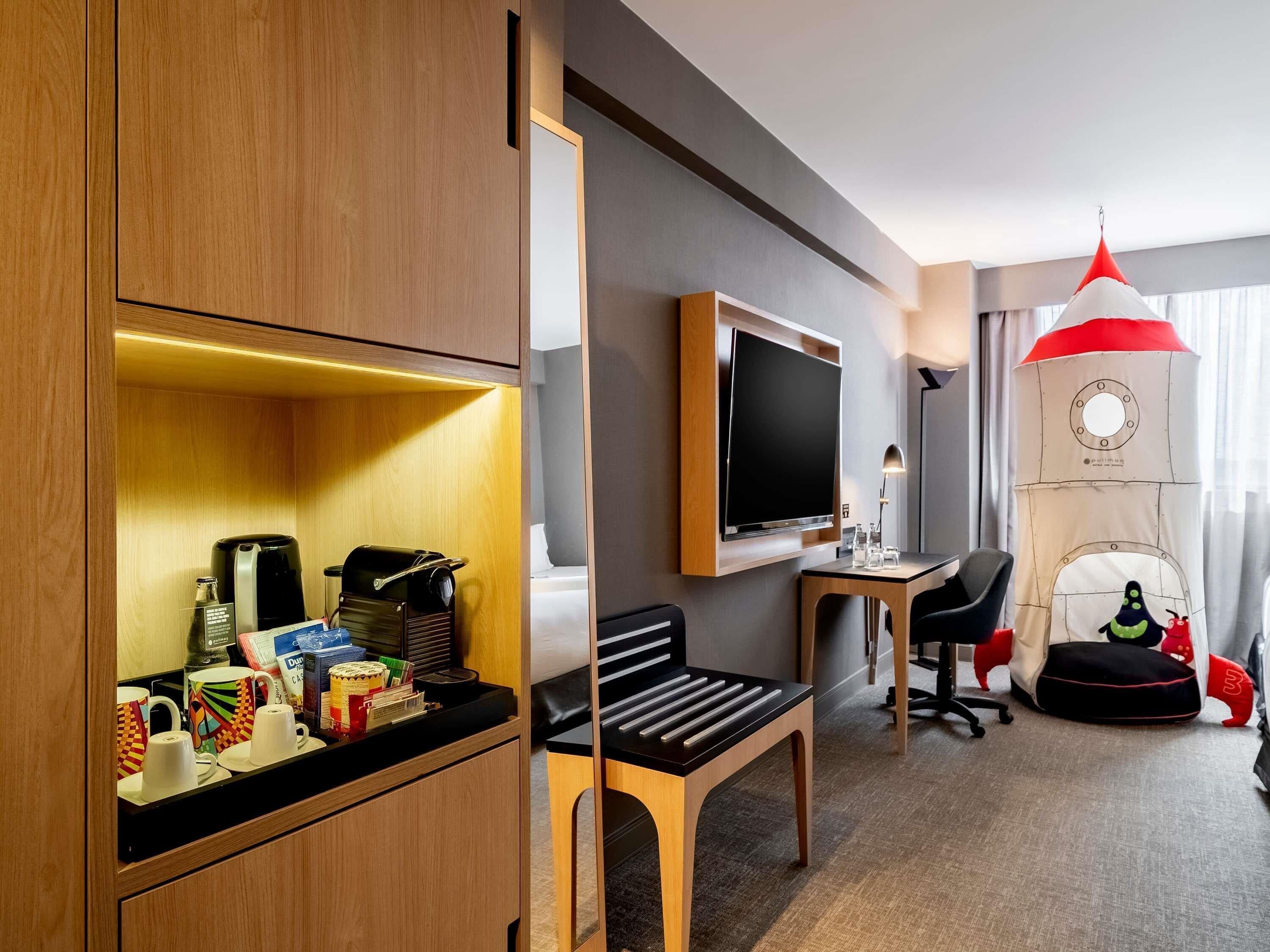 A hotel room with a wooden cabinet, a flat-screen TV, a desk with a chair, a pull-up bar, and a bed.