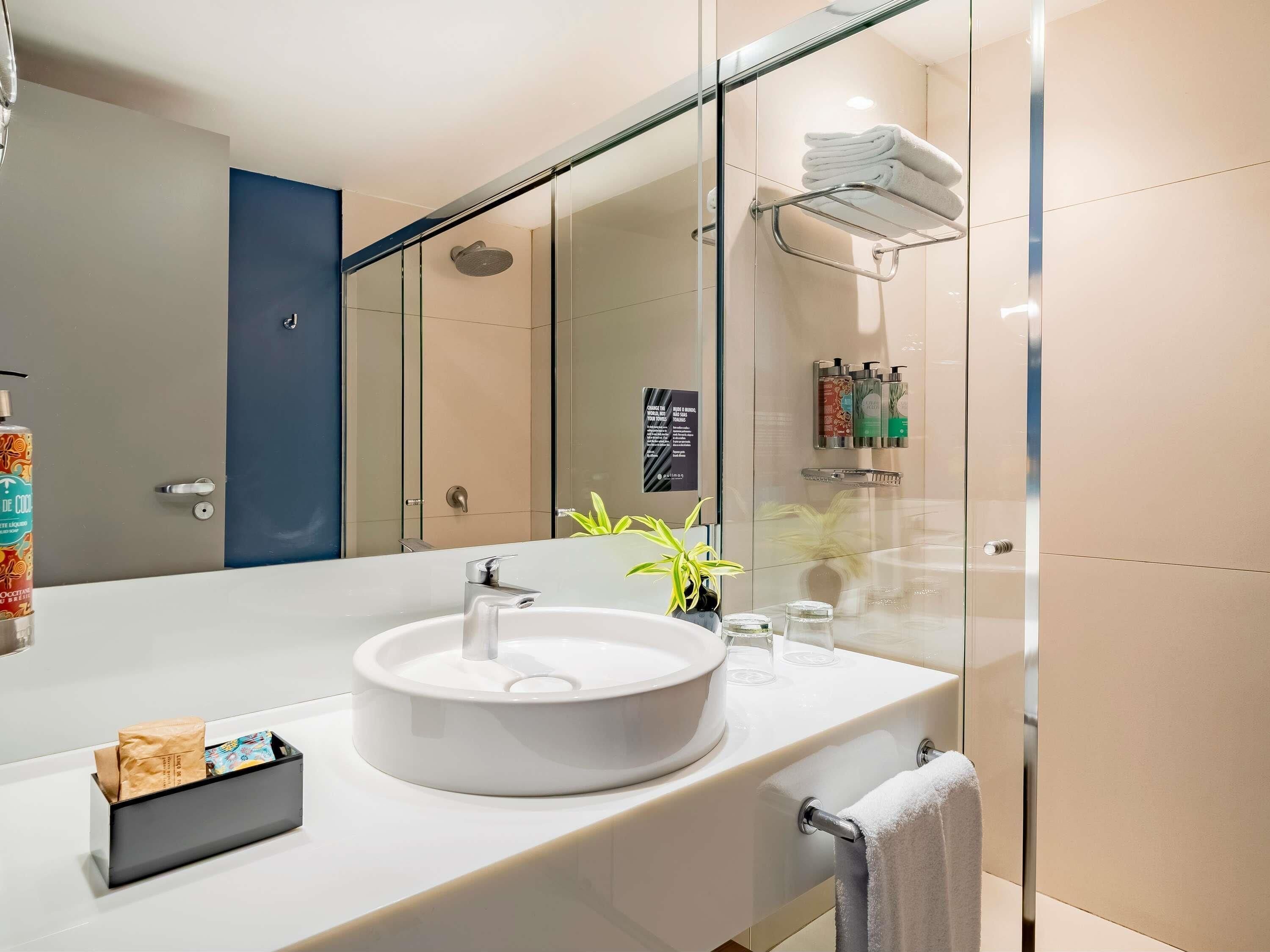 Un baño moderno con un espejo grande, un lavabo redondo, una cabina de ducha de vidrio y un perchero para toallas.