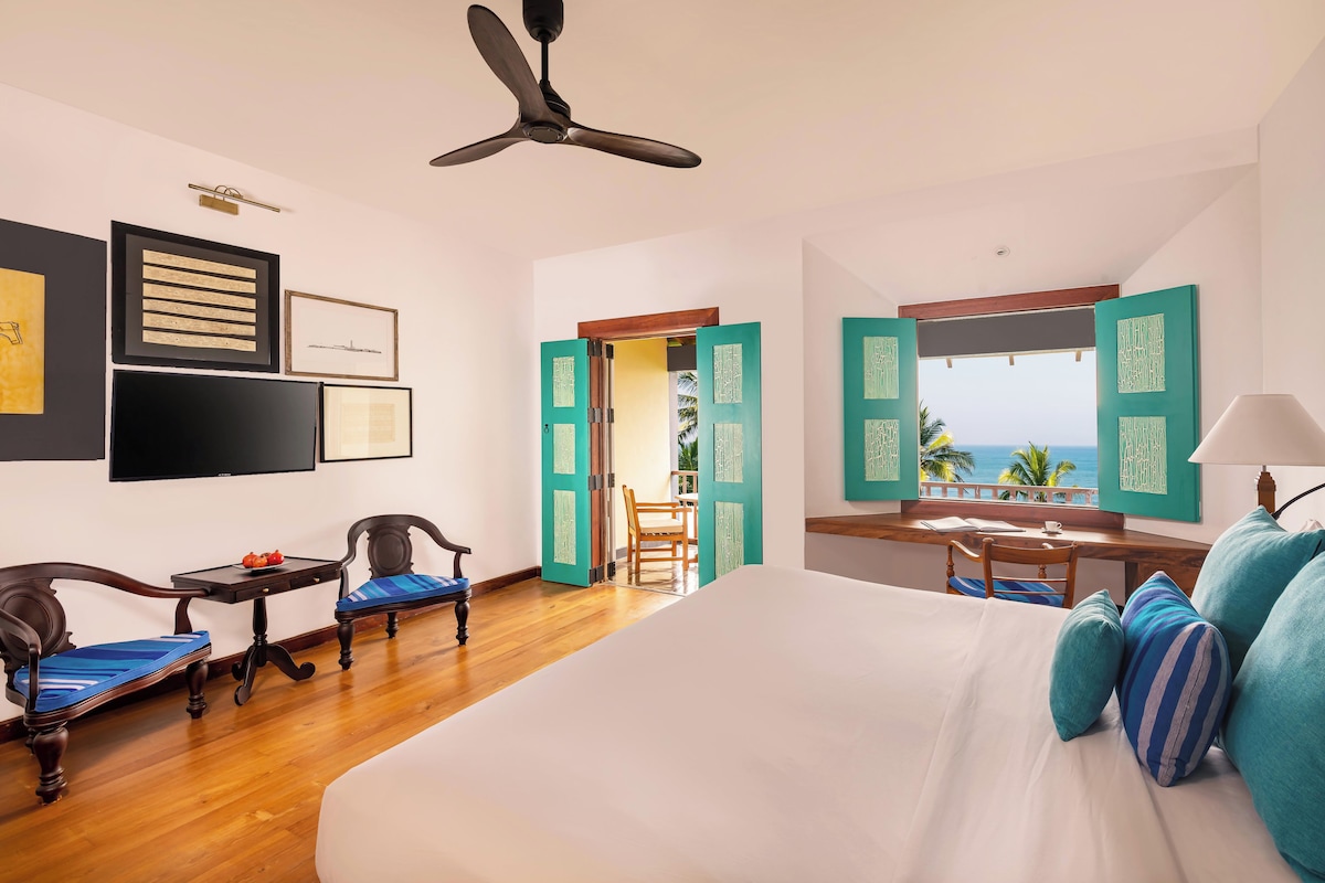 A hotel room with a large bed, a desk, two chairs, and a view of the ocean.