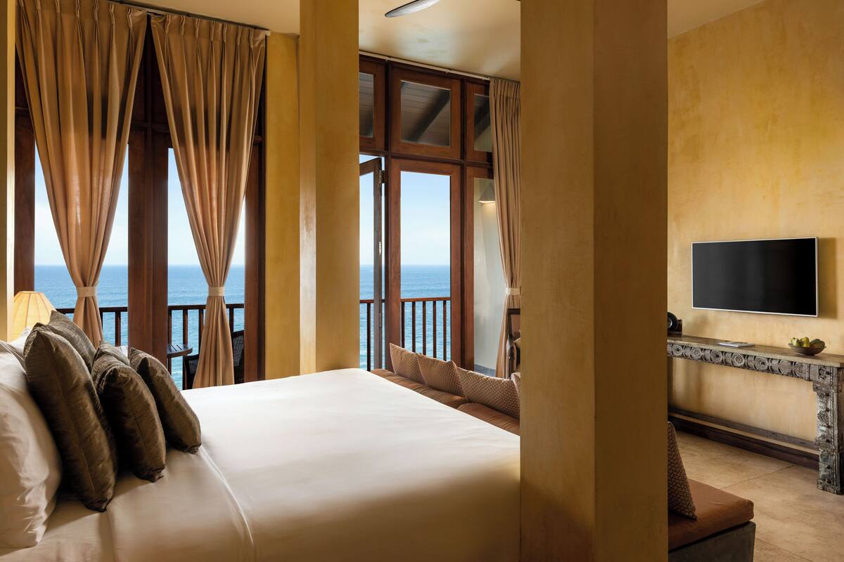 A bedroom with a large bed, curtains, a TV, and a view of the sea.