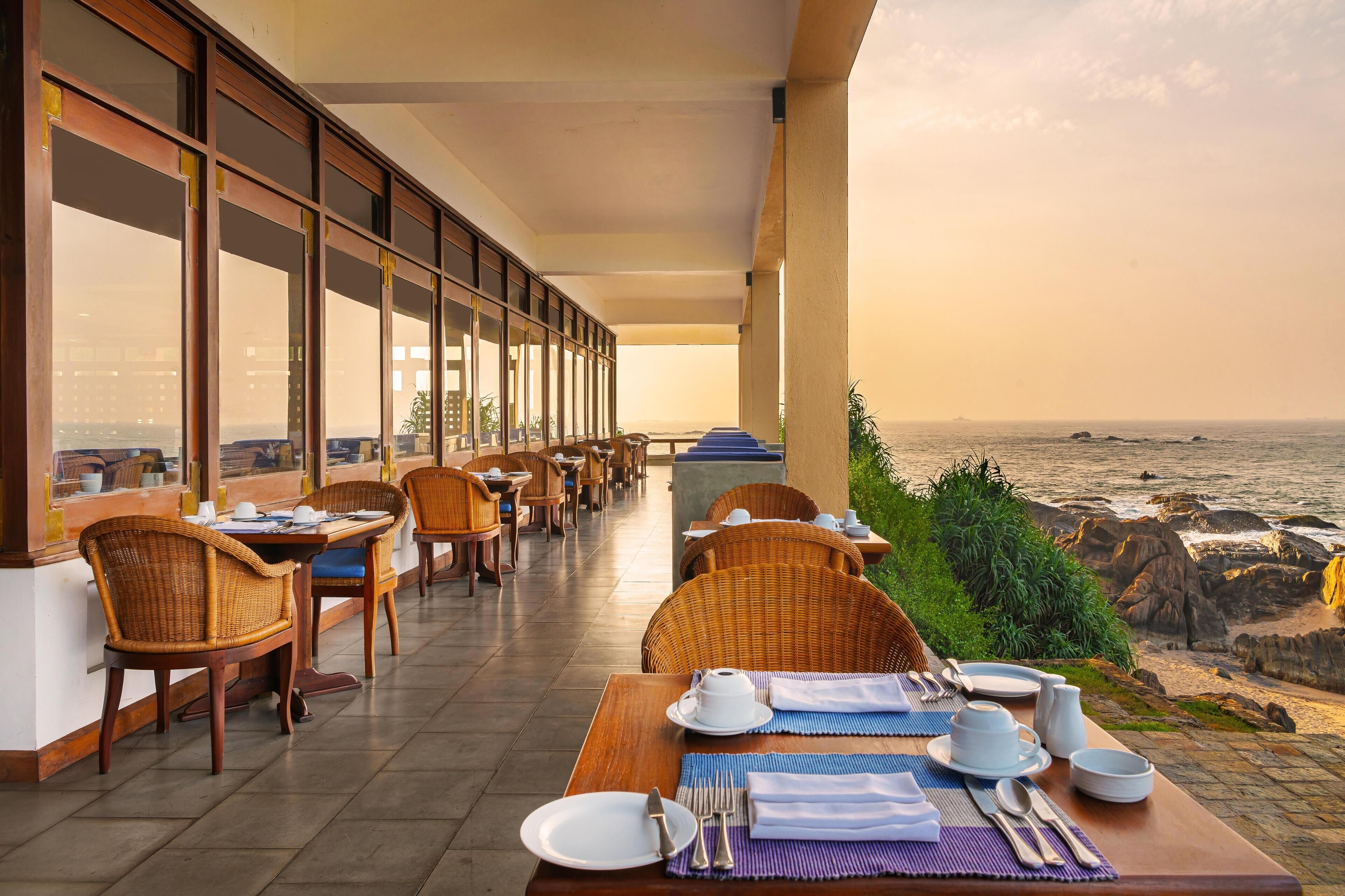 Un restaurante frente al mar con mesas y sillas, vista al océano y un litoral rocoso.