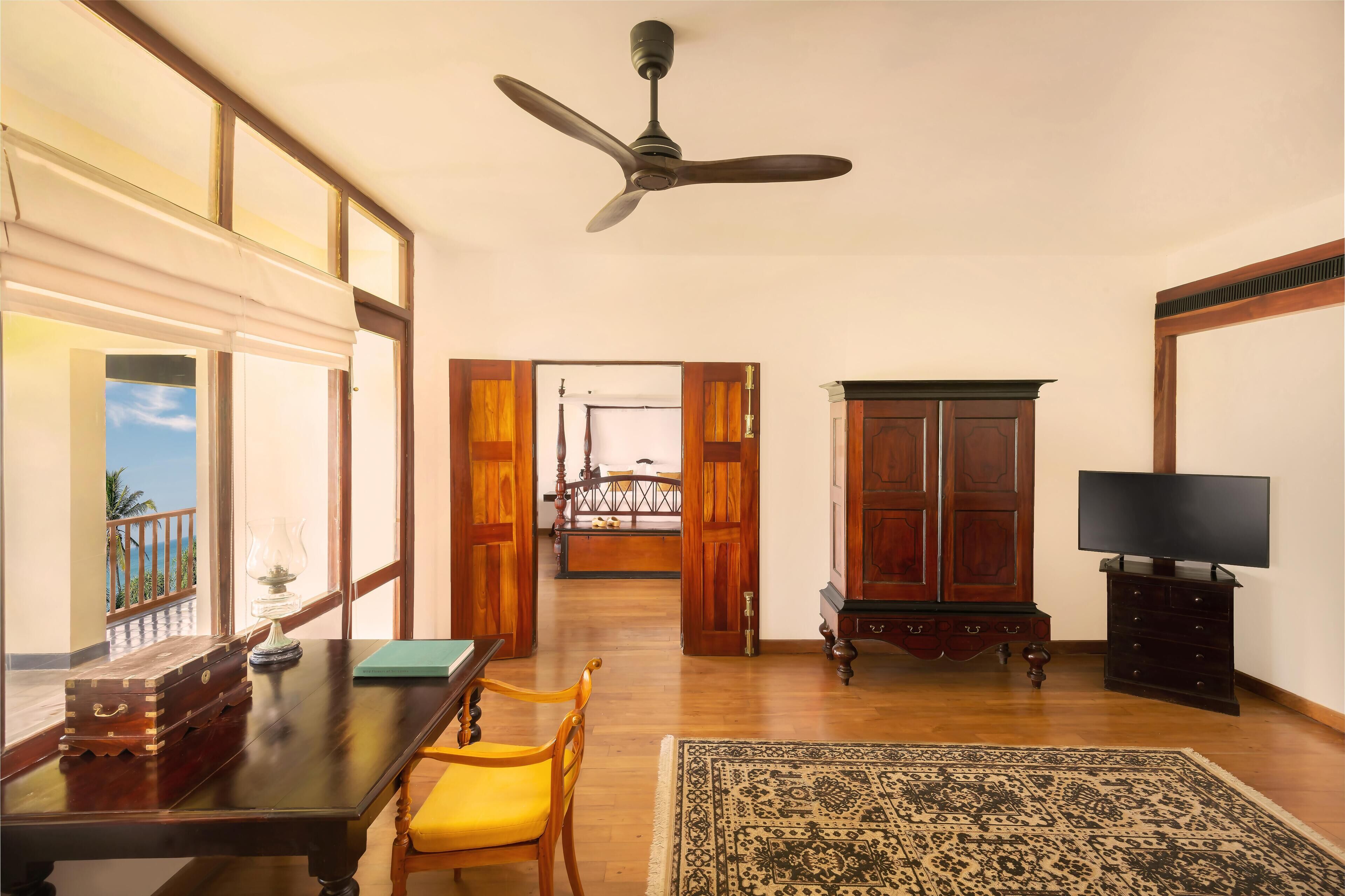 A room with a wooden table, a yellow chair, a television, and a ceiling fan.