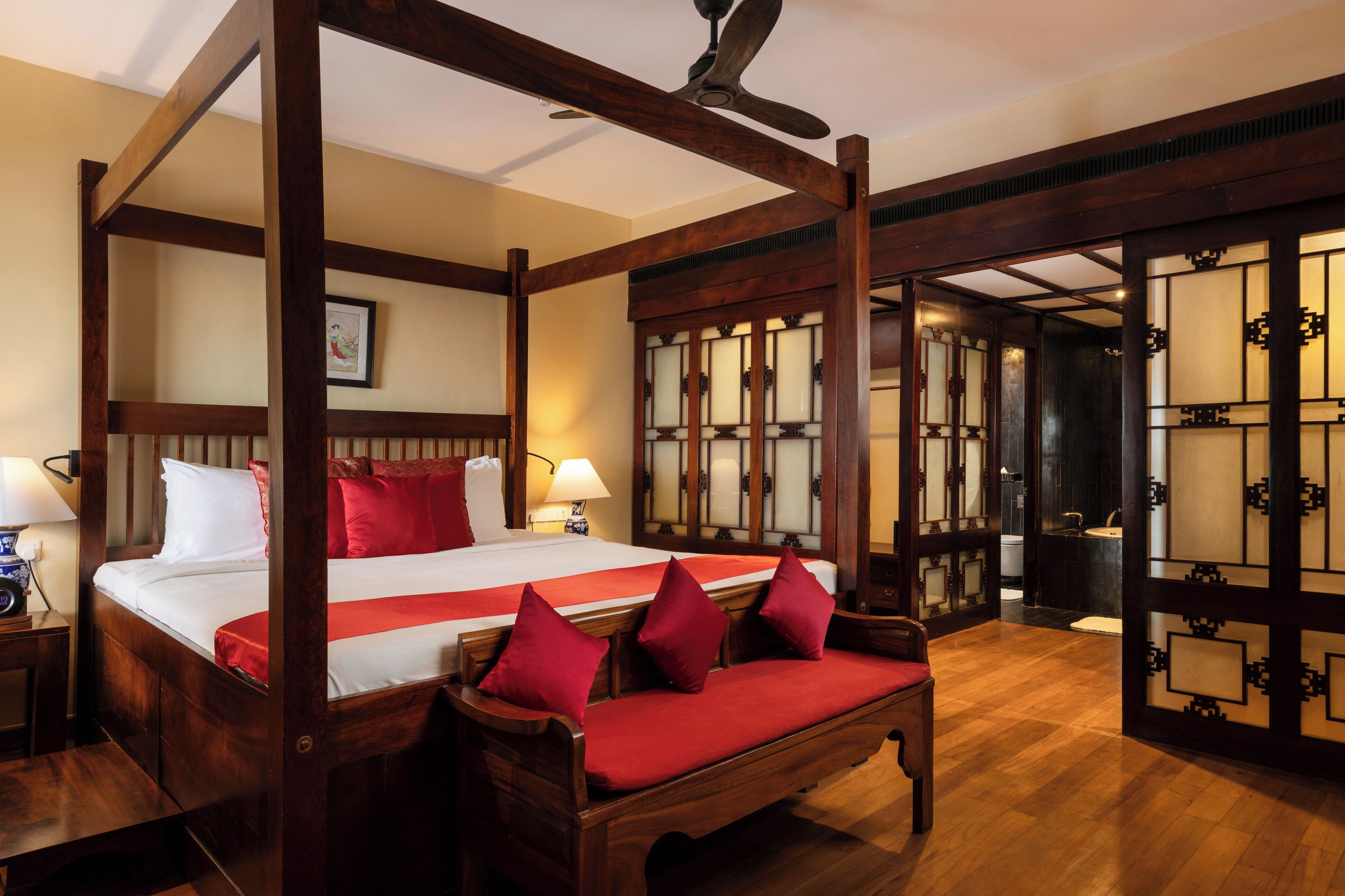 A four-poster bed with red pillows, wooden furniture, and a traditional design.