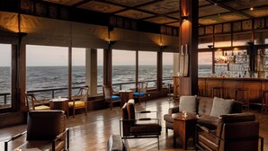 A bar area with wooden furniture, a bar counter, and large windows overlooking the sea. - Jetwing Lighthouse, A Luxury Reserve (Galle)