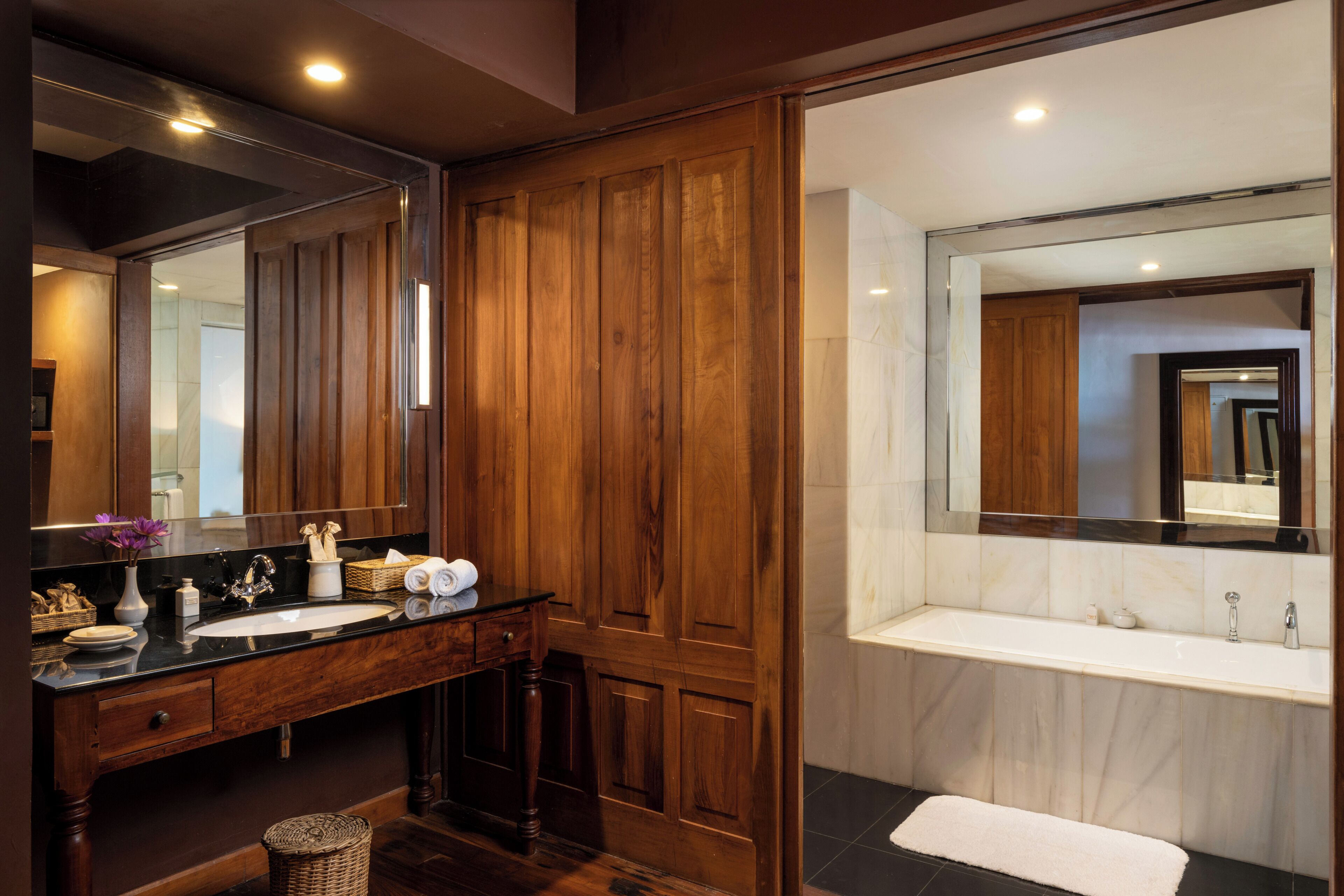 A modern bathroom with a wooden vanity, a large mirror, and a separate bathtub area.