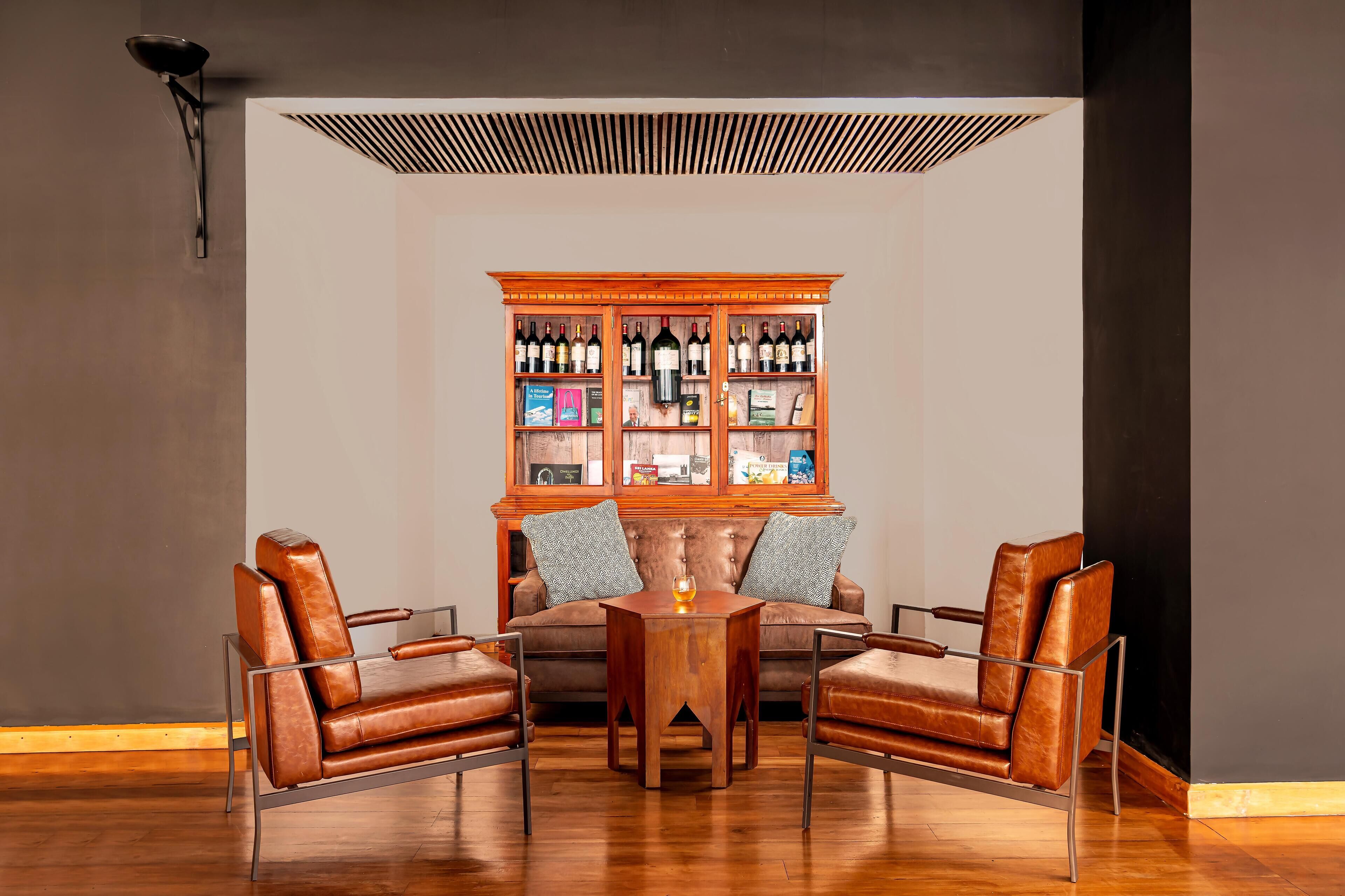 Uma sala de estar moderna com um aparador de madeira cheio de garrafas de vinho, poltronas de couro e uma mesa de vidro.