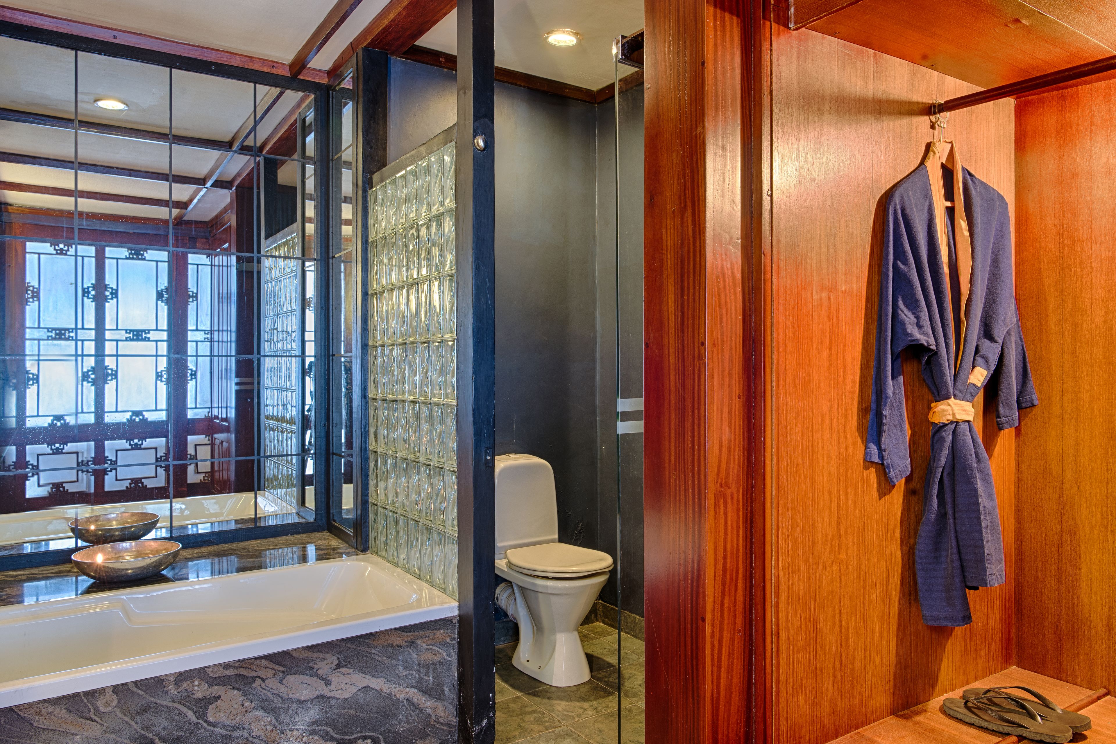 A bathroom with a bathtub, toilet, and wooden wall.