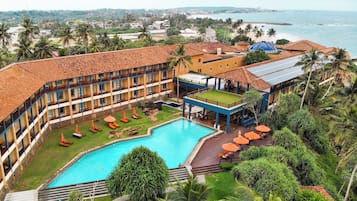 Relax by the pool surrounded by lush greenery and palm trees, with a view of the ocean and distant shoreline.