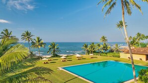 A pool area with a view of the ocean, surrounded by palm trees and lounge chairs. - Jetwing Lighthouse, A Luxury Reserve (Galle)