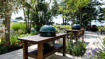 Un espace patio extérieur avec deux tables en bois, chacune surmontée d’un barbecue vert.