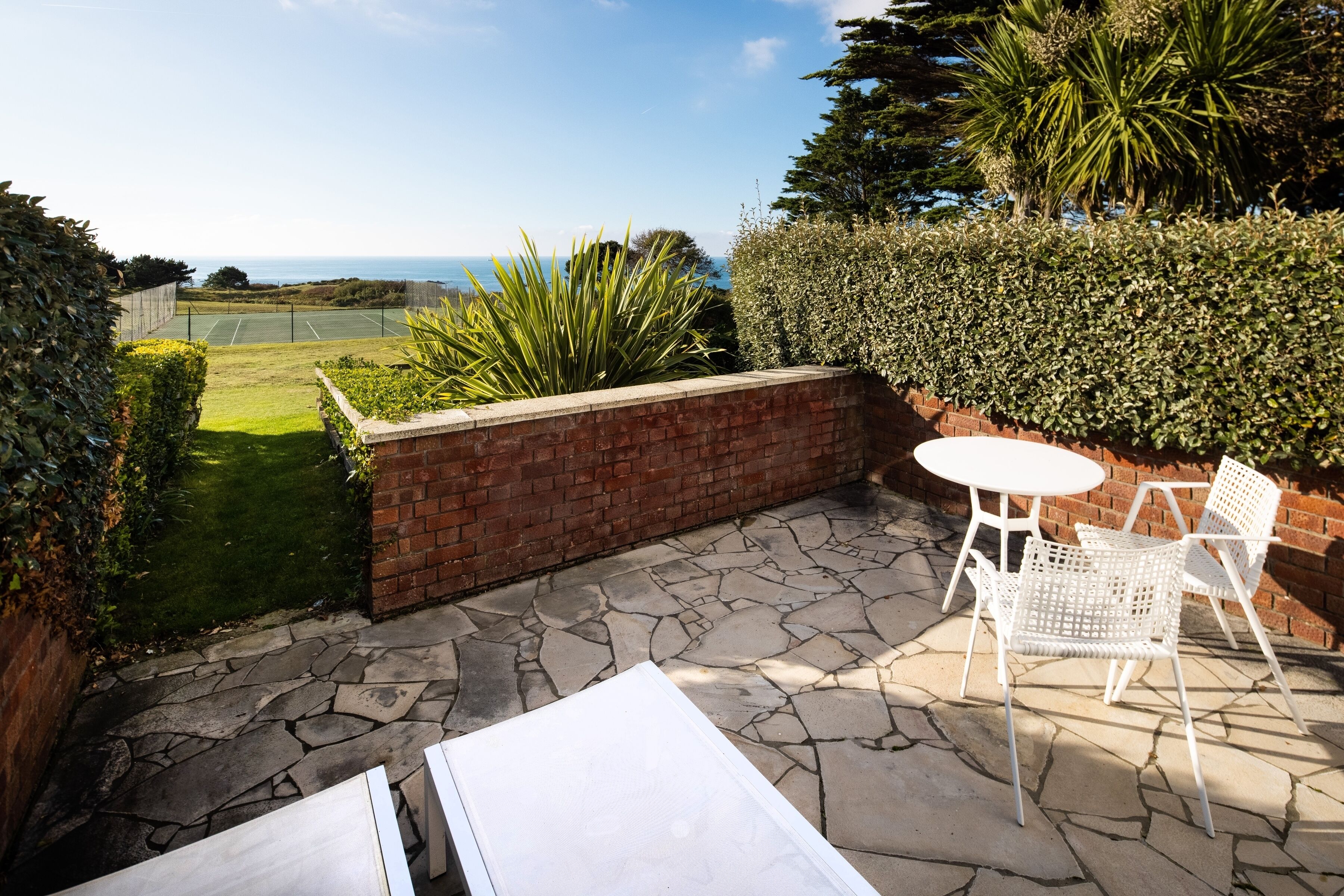 Un patio con pared de ladrillo, sillas blancas y una mesa.