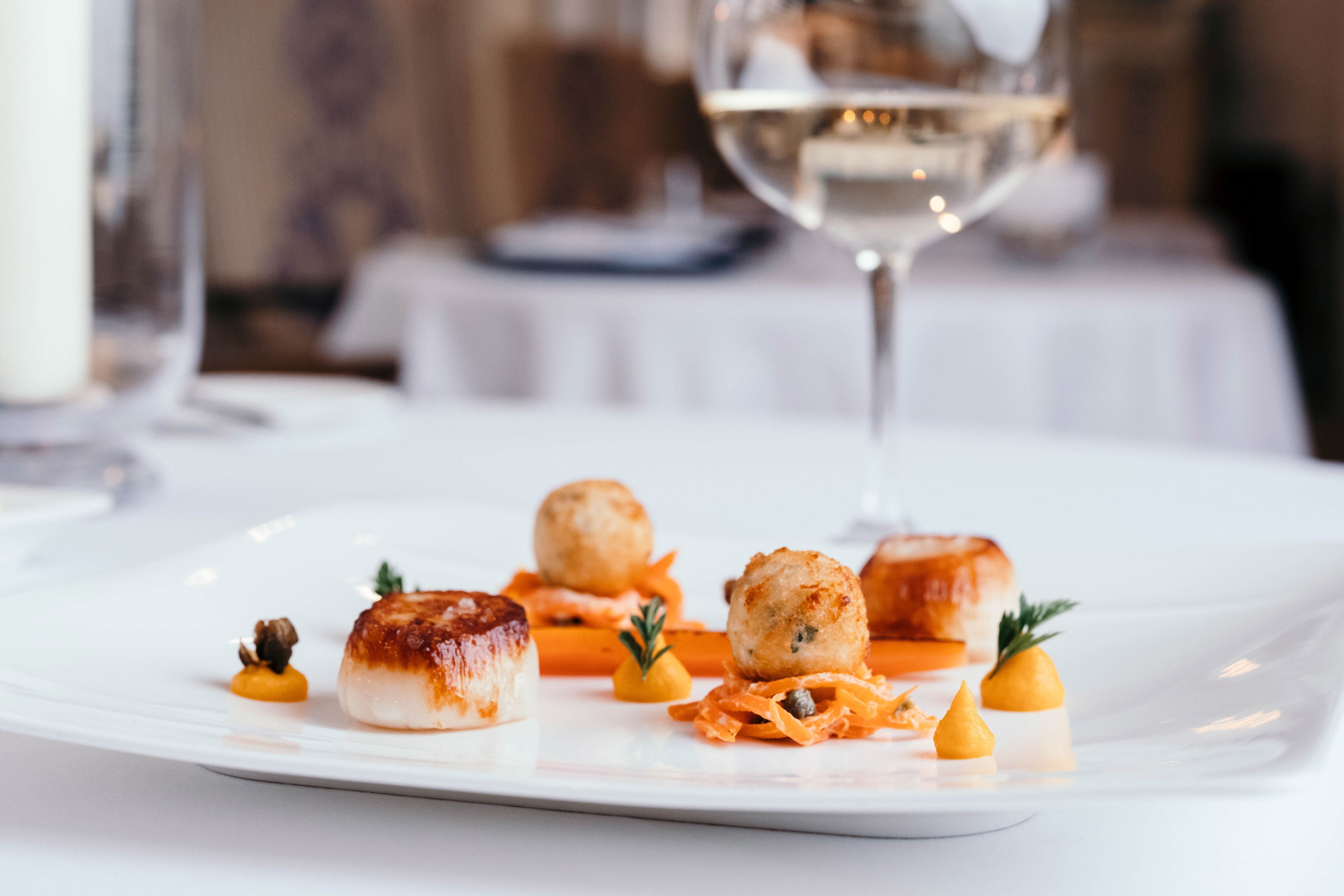 A white plate with various food items, a glass of white wine, and a candle in the background.