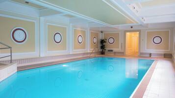 An indoor swimming pool with tiled walls, a tiled floor, and a door leading to another room.