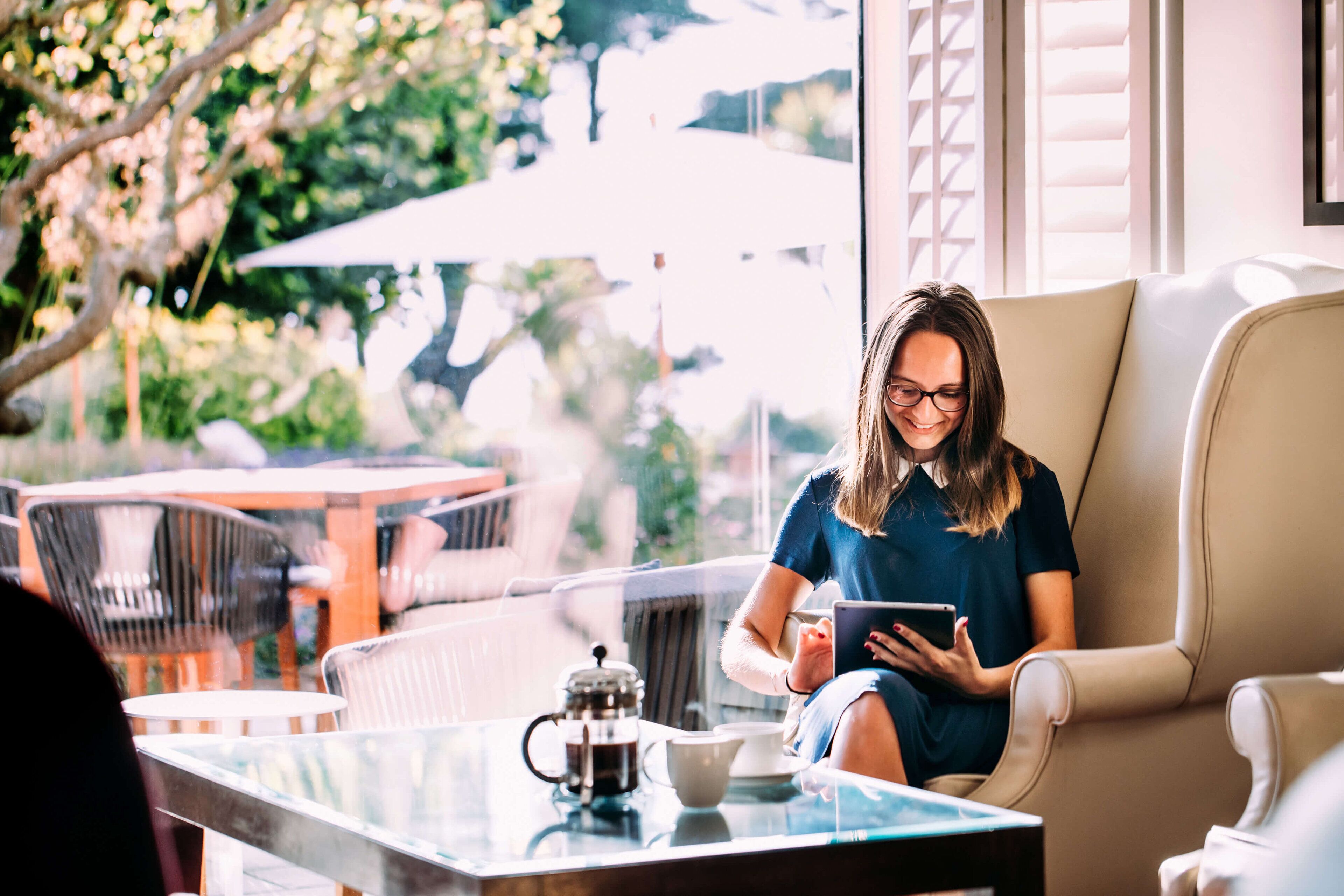 A person sitting on a beige sofa in a well-lit room with a glass table in front, holding a tablet.