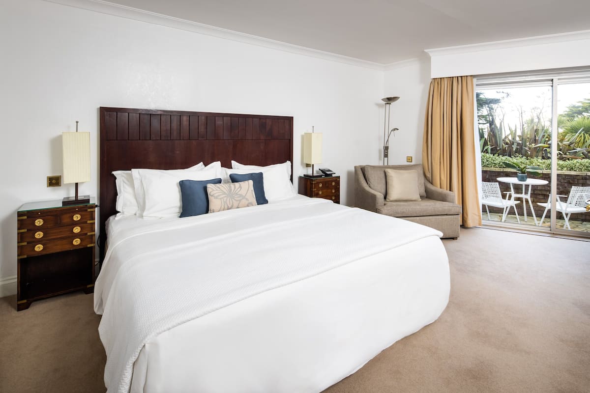 Habitación de hotel con una cama grande, dos mesitas de noche, una silla y vistas al exterior.