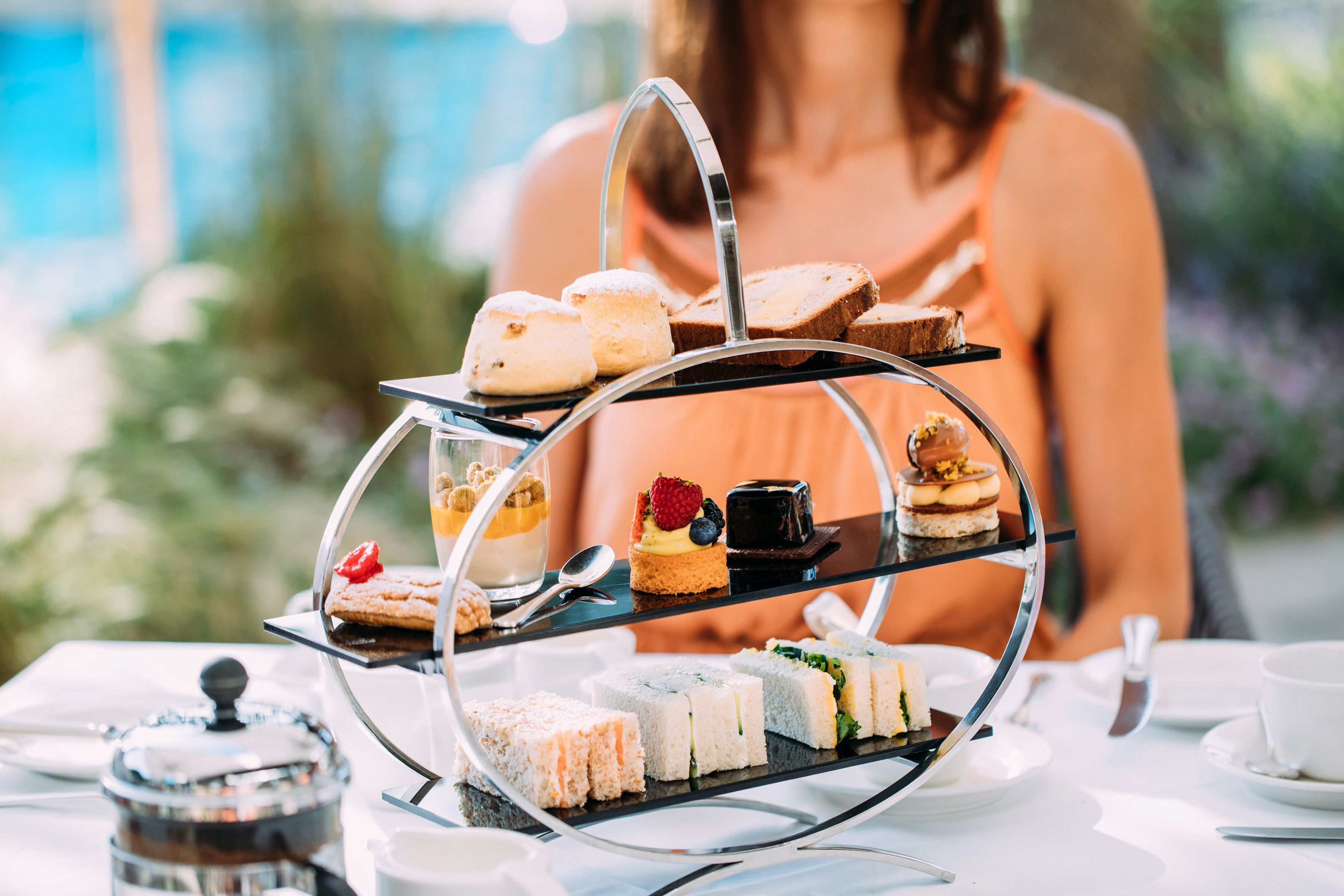 A three-tiered dessert stand with various pastries and sandwiches on a table.