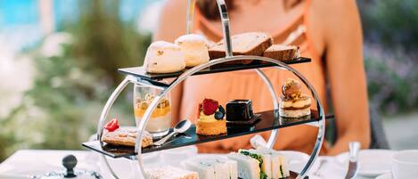A three-tiered dessert stand with various pastries and sandwiches on a table.