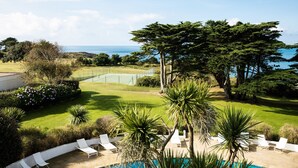 A poolside area with lounge chairs, a well-maintained lawn, and a tennis court in the background.