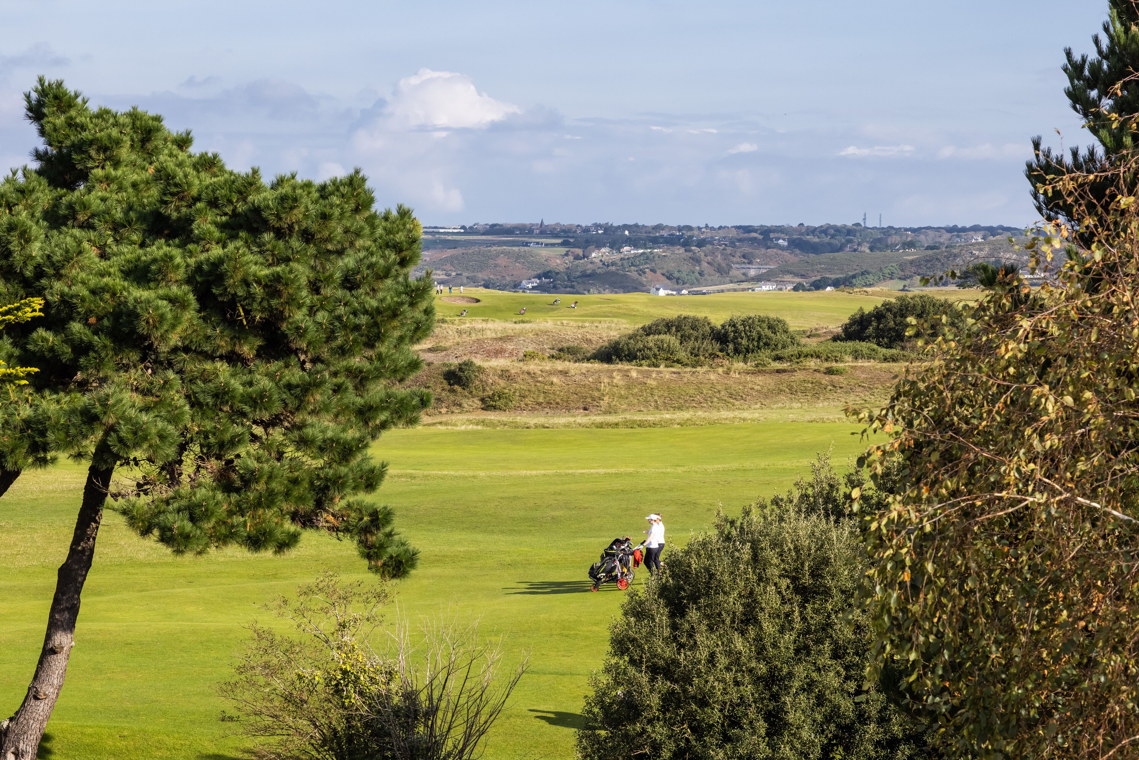 A golf course with a person walking a golf cart.