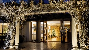 A hotel entrance with a covered patio, stone walls, and a Christmas tree inside.