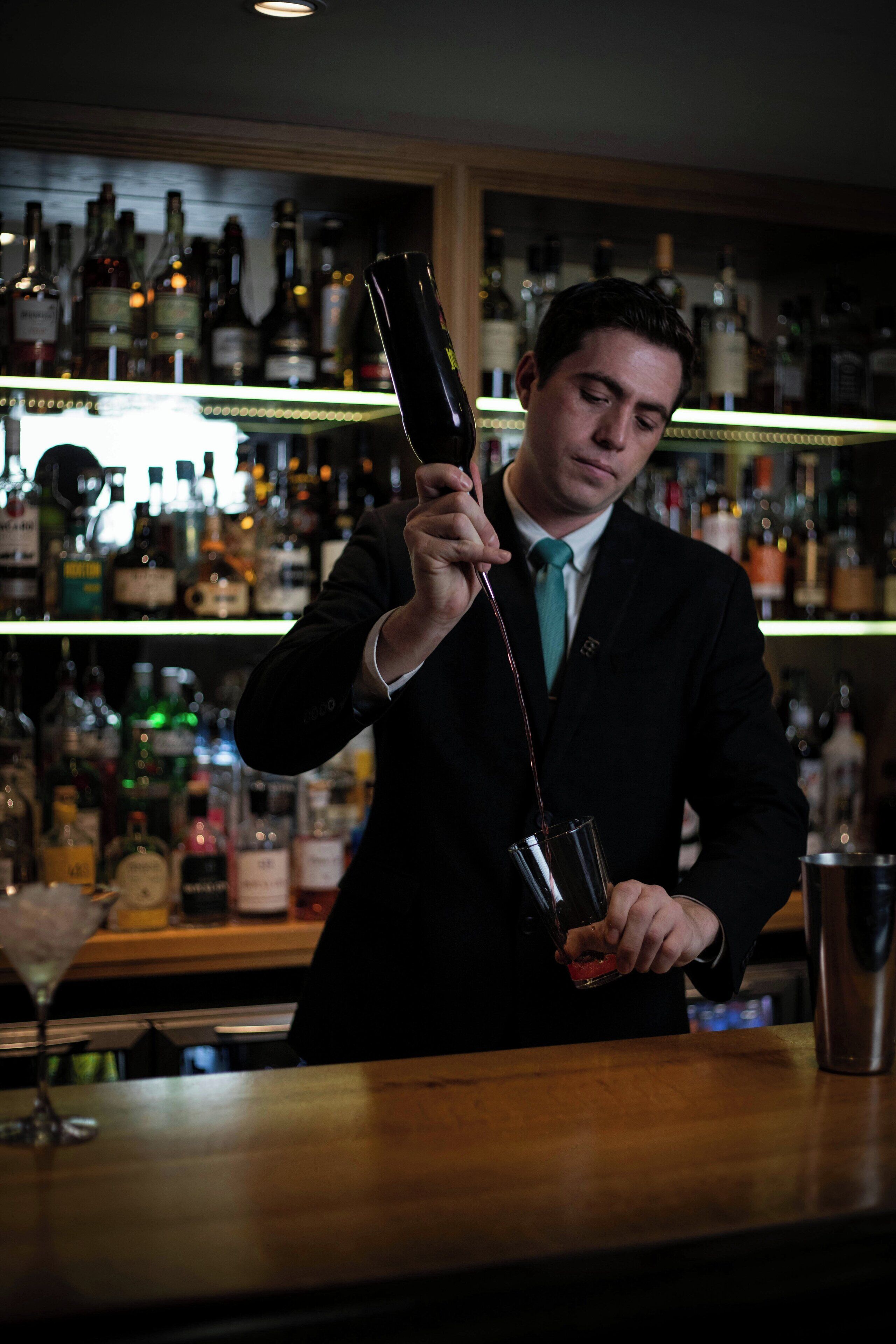 A bartender pouring a drink from a bottle into a glass.