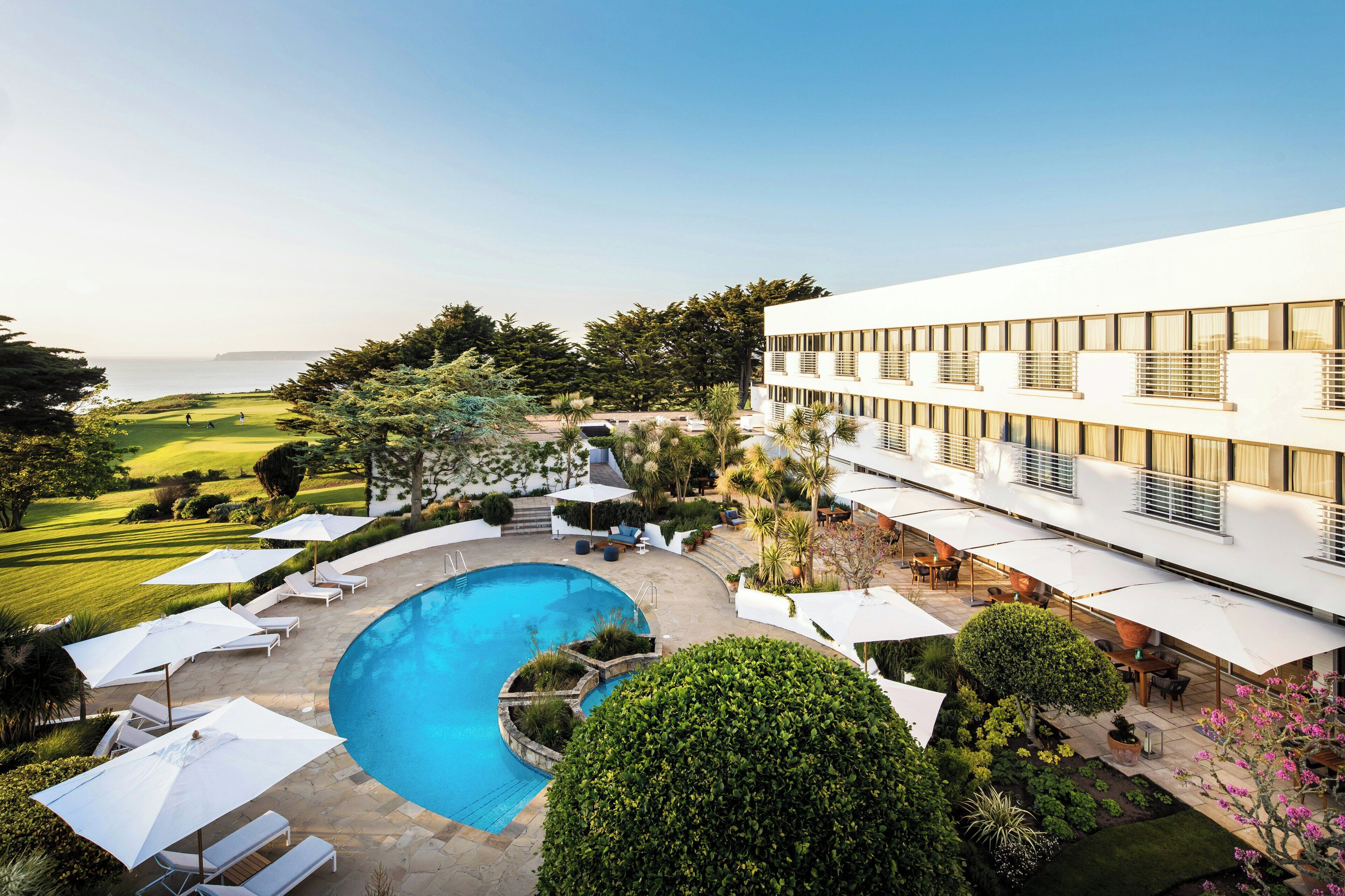 A modern hotel with a pool, outdoor seating, and a view of the ocean.