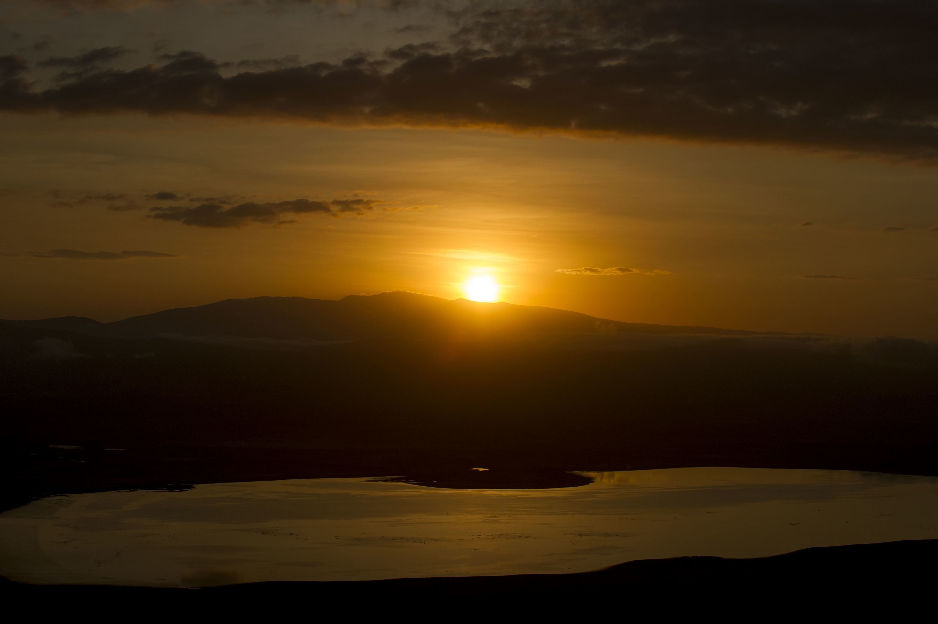 A sunset over a mountainous landscape with a body of water in the foreground.