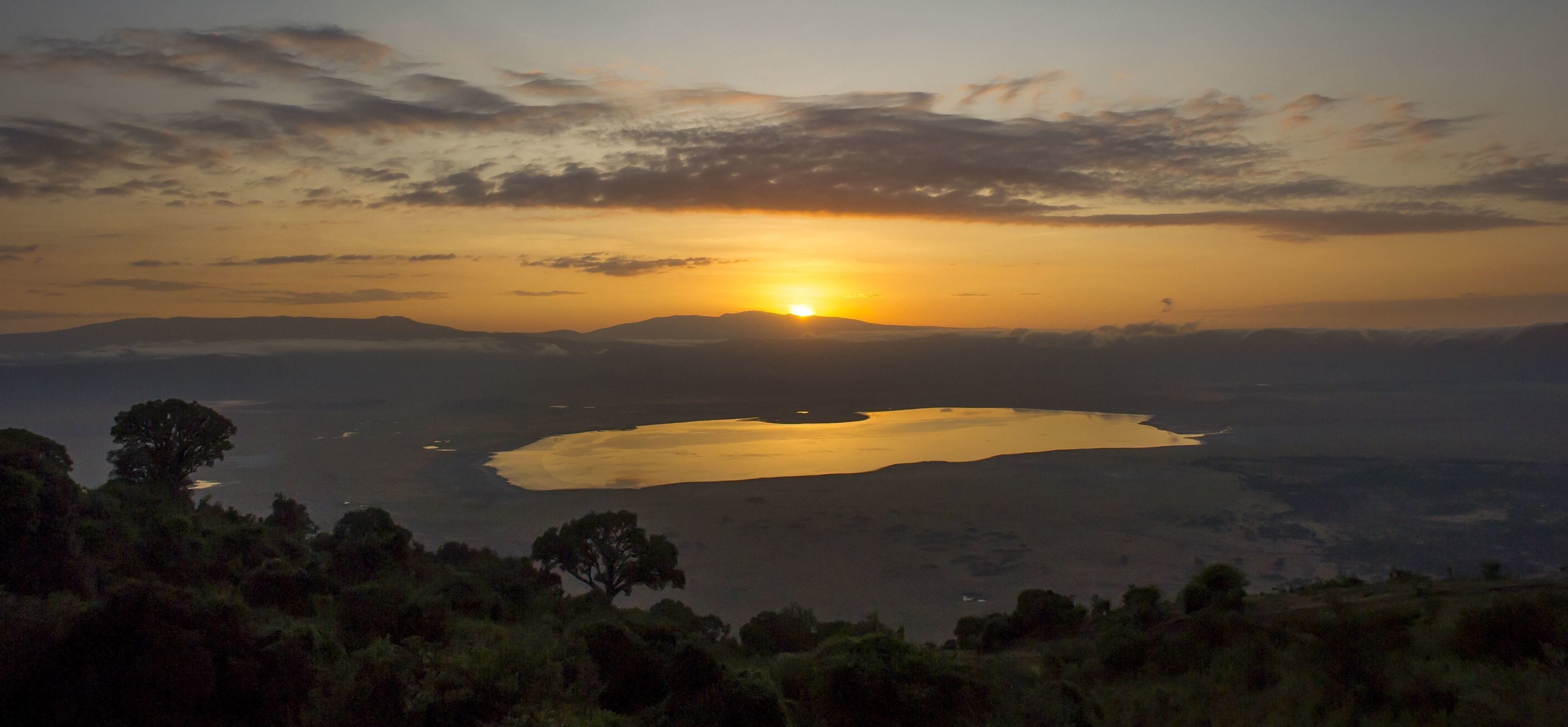 A sunset over a lake with surrounding hills and trees.