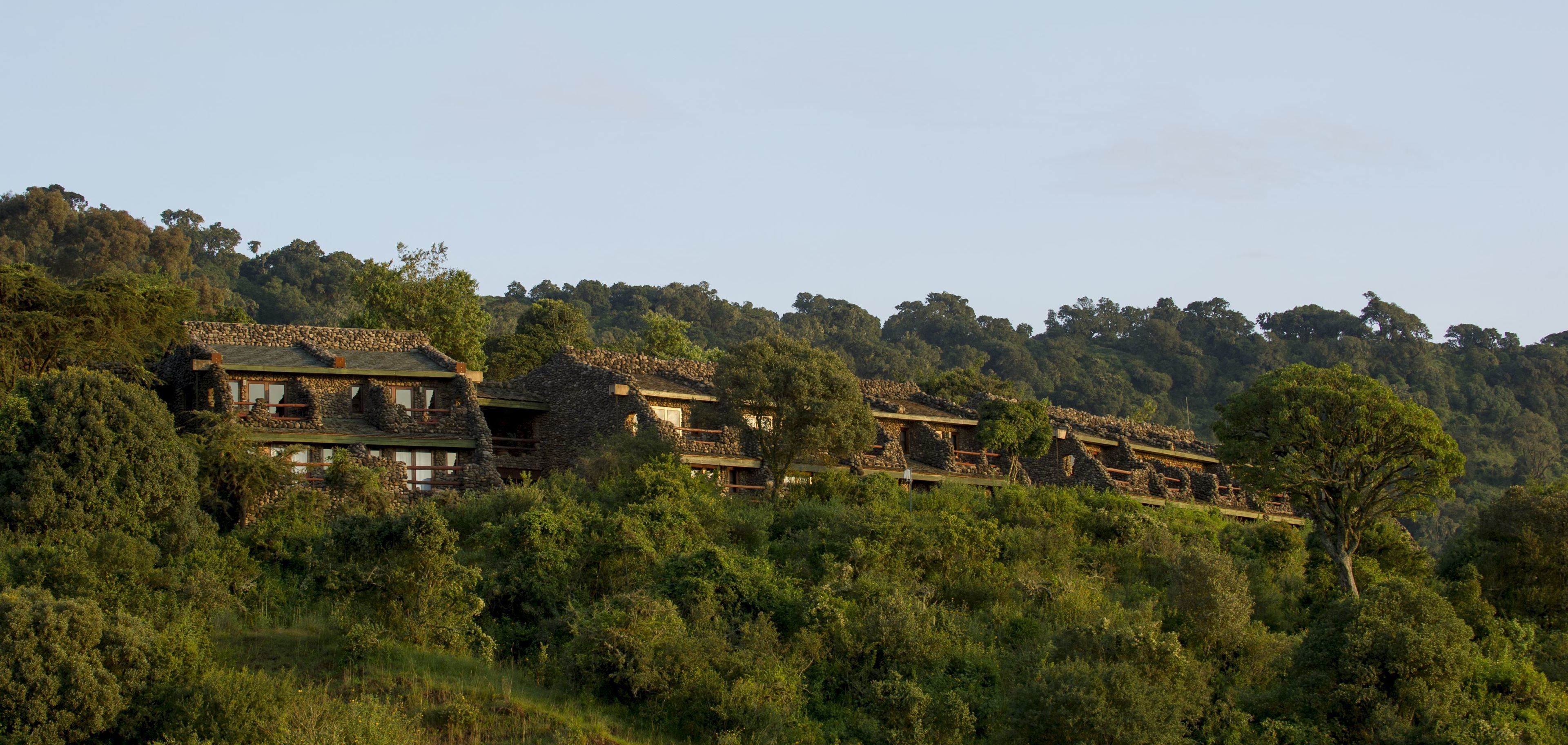 Un bâtiment en pierre doté de nombreux balcons, entouré d’une forêt dense et de collines.