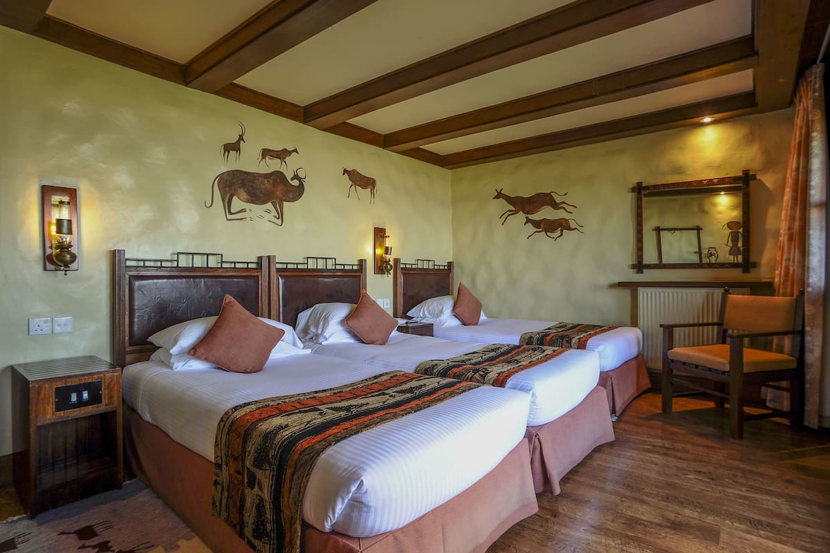 A room with three beds, wooden headboards, and a large mirror.