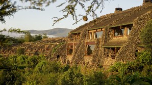Um edifício de pedra com várias divisões, rodeado por vegetação exuberante e colinas ao fundo.