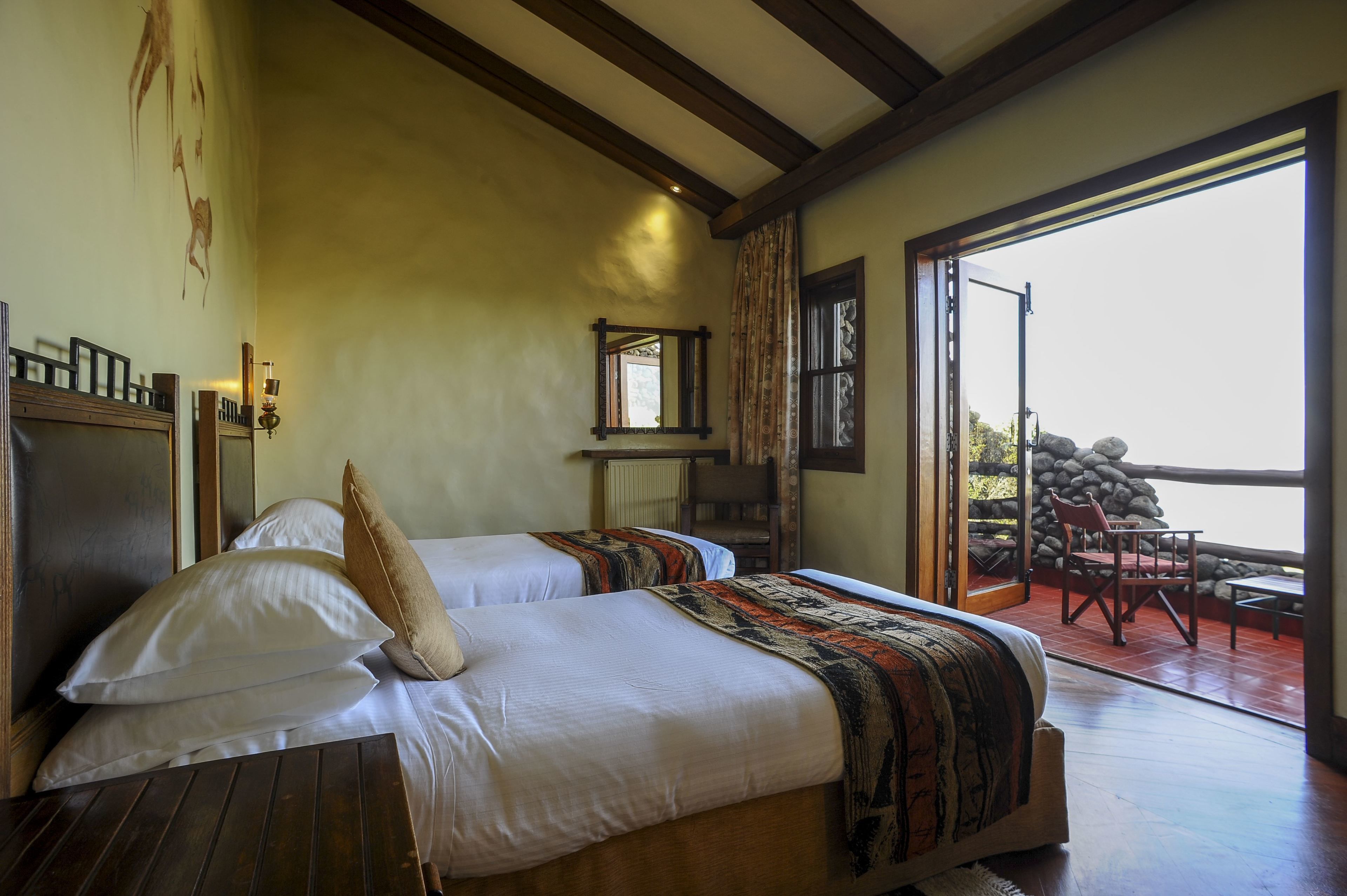 A bedroom with two beds, a wooden ceiling, a large window, and a view of a stone wall outside.