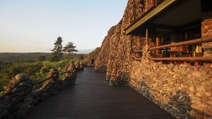 Edifício com paredes de pedra e um deque de madeira que leva a um espaço coberto.