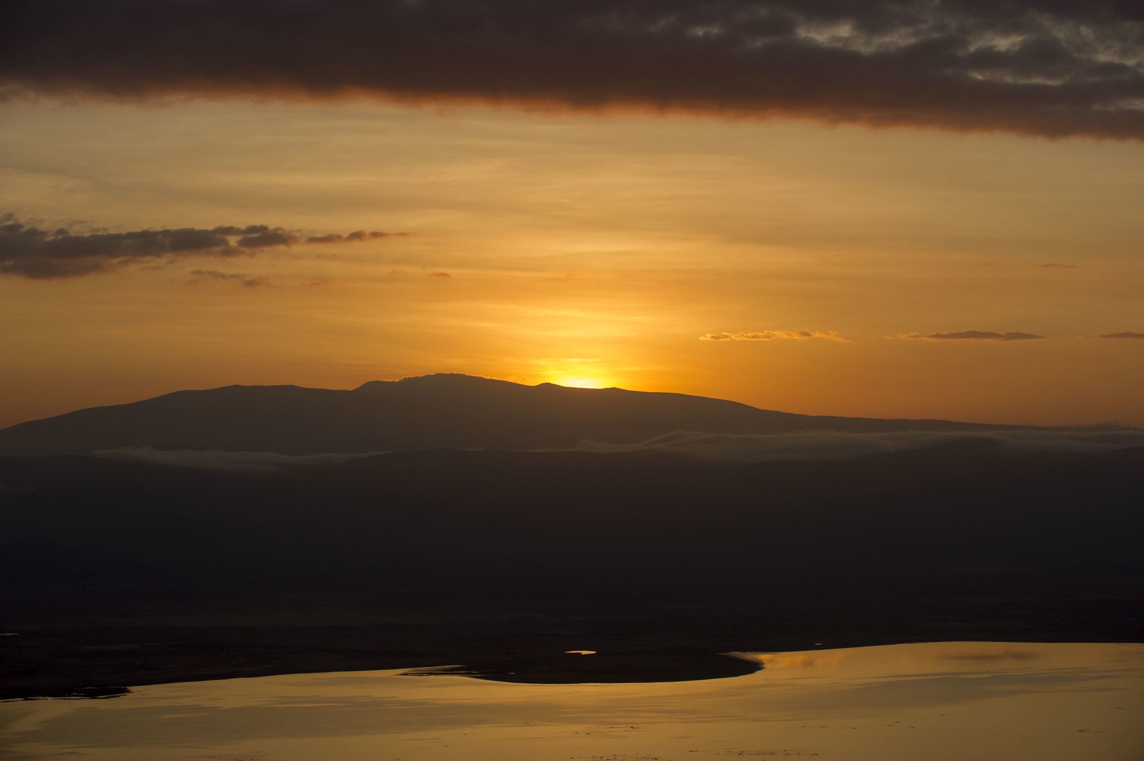 A mountain silhouette at sunset with a lake in the foreground.