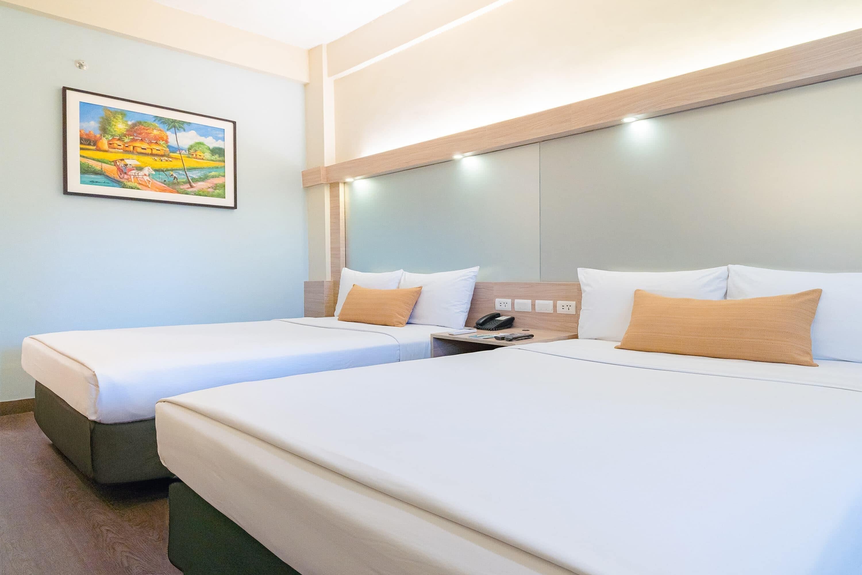 Una habitación de hotel con dos camas, un cuadro en la pared y una mesita de noche con un teléfono y una lámpara.