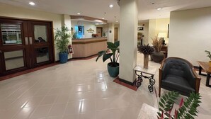 A hotel reception area with a reception desk, a waiting area with a sofa and chairs, and potted plants. - Microtel by Wyndham Tarlac (Tarlac)
