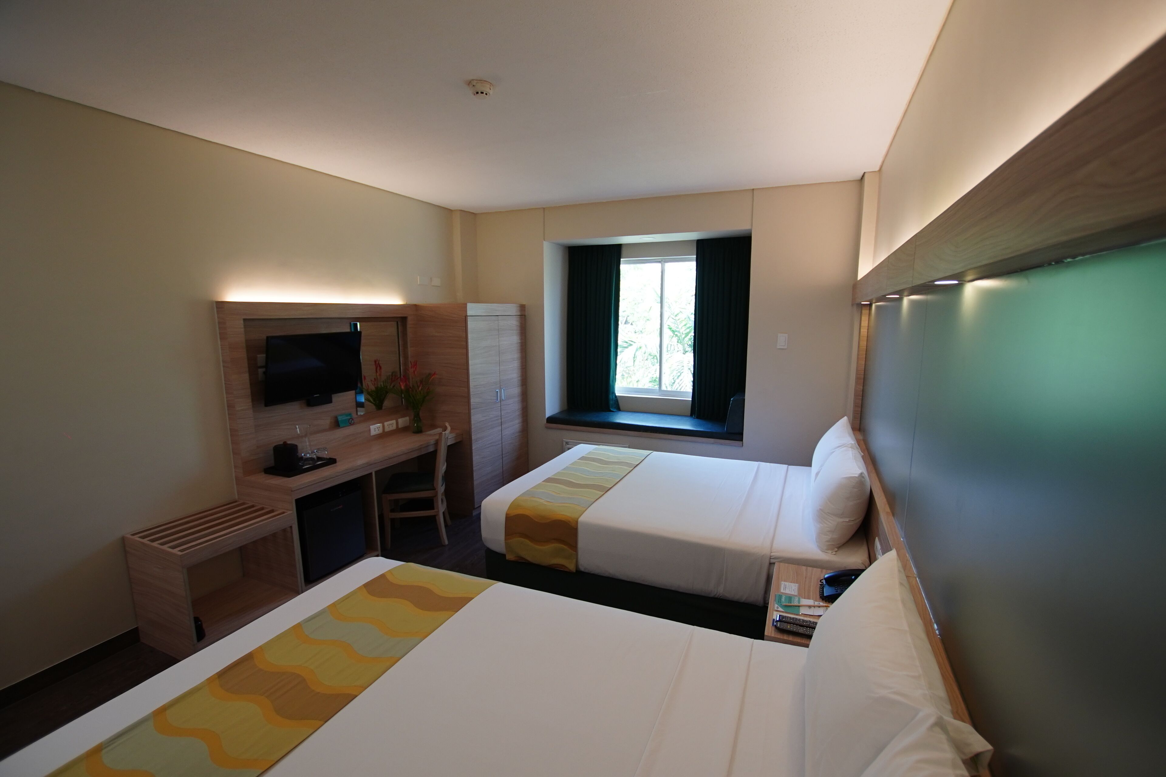 A hotel room with two beds, a desk with a computer, a TV, and a window with curtains.