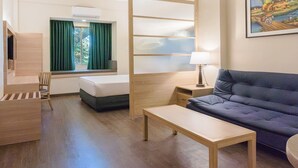 A hotel room with a bed, a sofa, a desk, a chair, a window with curtains, a lamp, and a painting on the wall. - Microtel by Wyndham Tarlac (Tarlac)