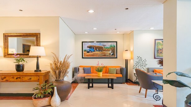 A hotel lobby with a wooden reception desk, a sofa with orange cushions, a coffee table, and a painting of a truck on the wall. - Microtel by Wyndham Tarlac (Tarlac)